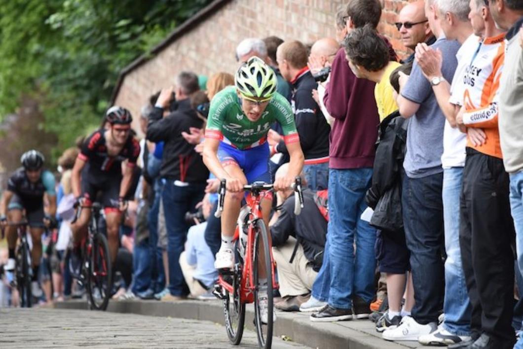 Racing cyclists, three, lead rider in green jersey and blue shorts, cobbled hill, brick wall on one side lined with spectators, Dan Pearson, 